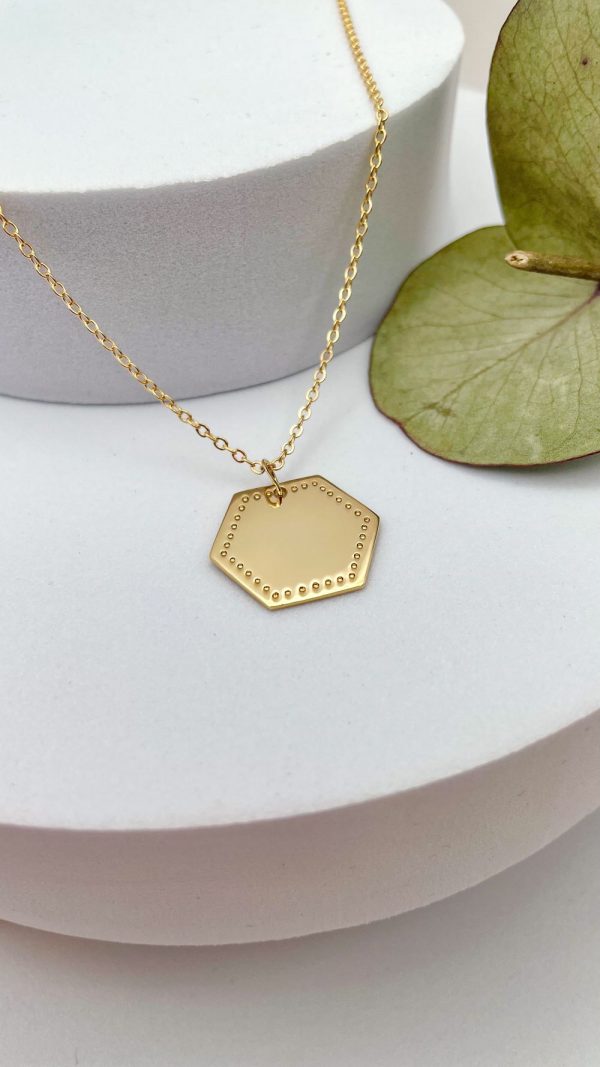 Collier médaille hexagonale en plaqué or posé sur fond blanc, bijou personnalisable et raffiné