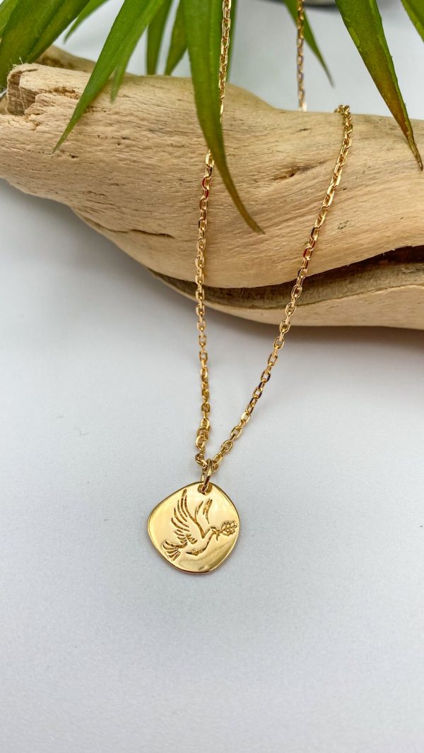 Collier plaqué or avec pendentif colombe posé sur bois clair, bijou symbolique chrétien