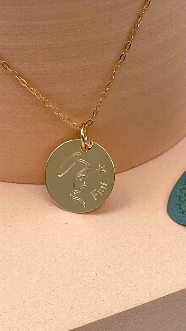 Collier Vierge Marie Fiat en plaqué or avec gravure "Fiat", posé sur support beige, bijou religieux fin et moderne