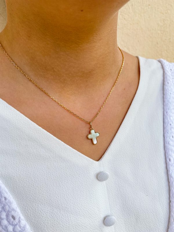 Collier croix en nacre blanche porté sur une blouse blanche - bijou chrétien élégant et épuré