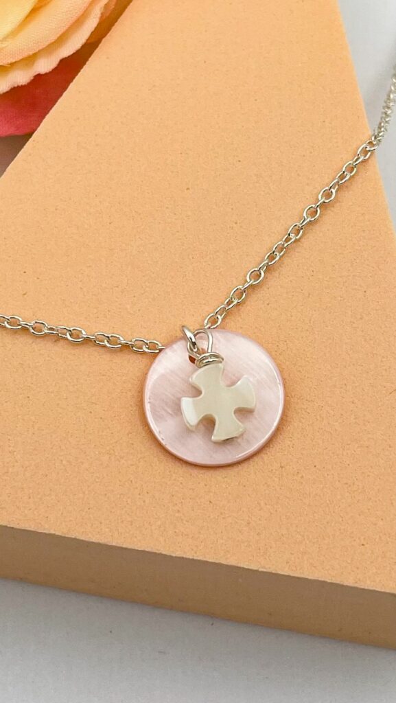Gros plan sur le pendentif catho : croix en nacre blanche sur médaille ronde rose, monté sur chaîne en argent