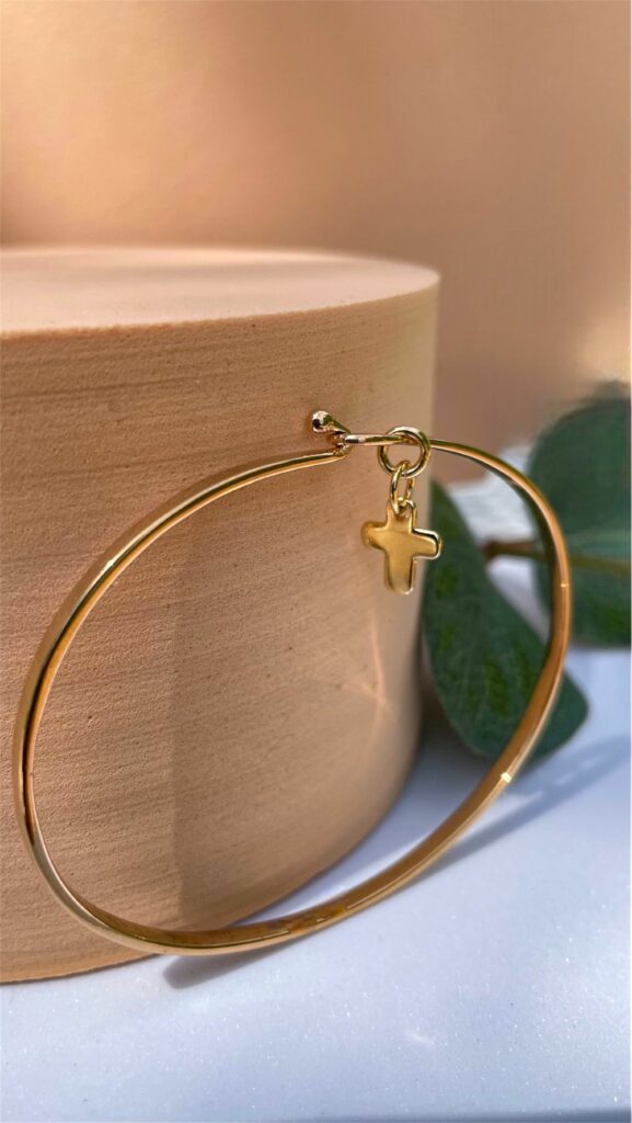 Bracelet jonc doré avec petite croix suspendue sur support beige – bijou religieux raffiné