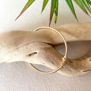 Bracelet jonc torsadé en plaqué or déposé sur une branche de bois flotté – bijou doré chic et intemporel pour femme