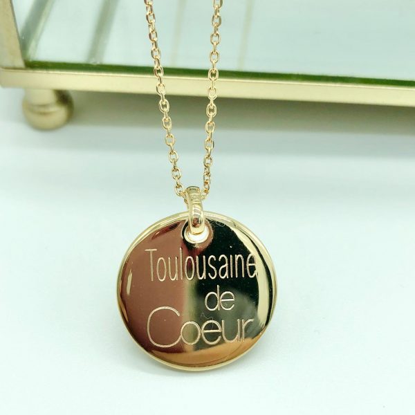 Collier personnalisé Toulousaine de Cœur en plaqué or, présenté devant une boîte en verre doré