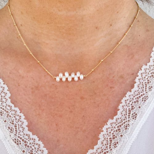 Collier en plaqué or avec perles d'eau douce blanches montées en ligne, porté sur un décolleté blanc en dentelle. Bijou élégant pour mariage, cérémonie ou tenue de fête.