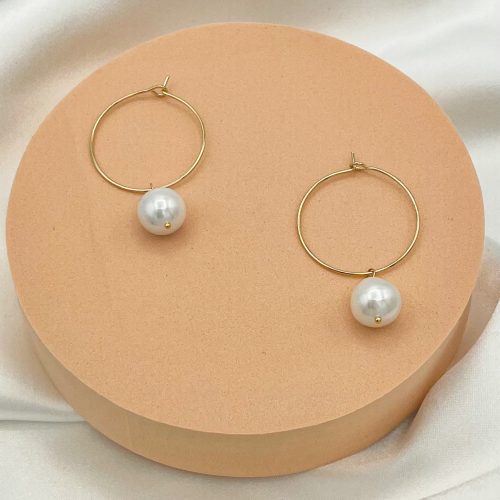 Boucles d’oreilles créoles en plaqué or avec véritables perles de culture blanches d’eau douce, présentées sur un support beige. Bijou élégant pour mariage, cérémonie et tenue raffinée.