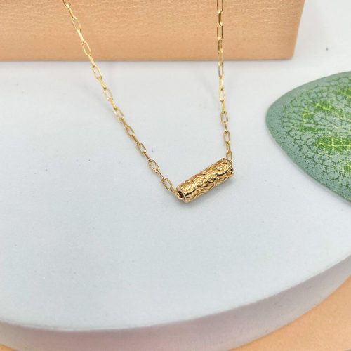 Collier tube balinais en plaqué or texturé mis en lumière sur fond naturel, bijou raffiné de la collection Gili