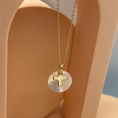 Collier croix chrétien sur nacre blanche avec chaîne fine plaqué or présenté sur support beige, bijou religieux moderne femme élégant