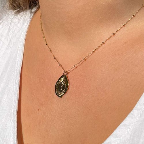 Collier croix rayonnante plaqué or porté femme avec médaille irrégulière et chaîne fine, bijou chrétien moderne discret.