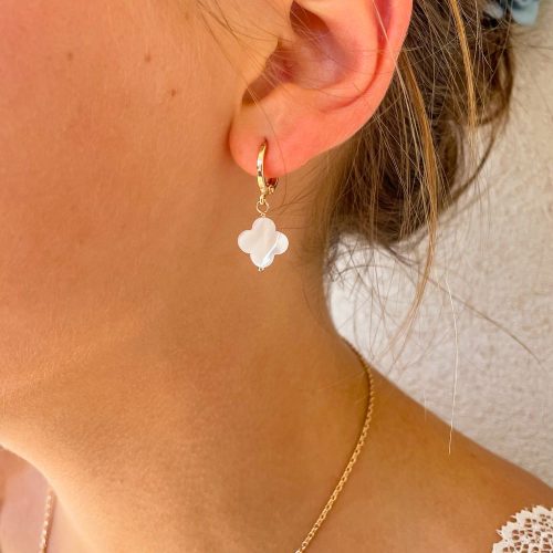 Jeune femme portant des boucles d’oreilles créoles fines en plaqué or avec pendentif trèfle en nacre blanche, bijou élégant et lumineux pour mariage, communion ou cérémonie.